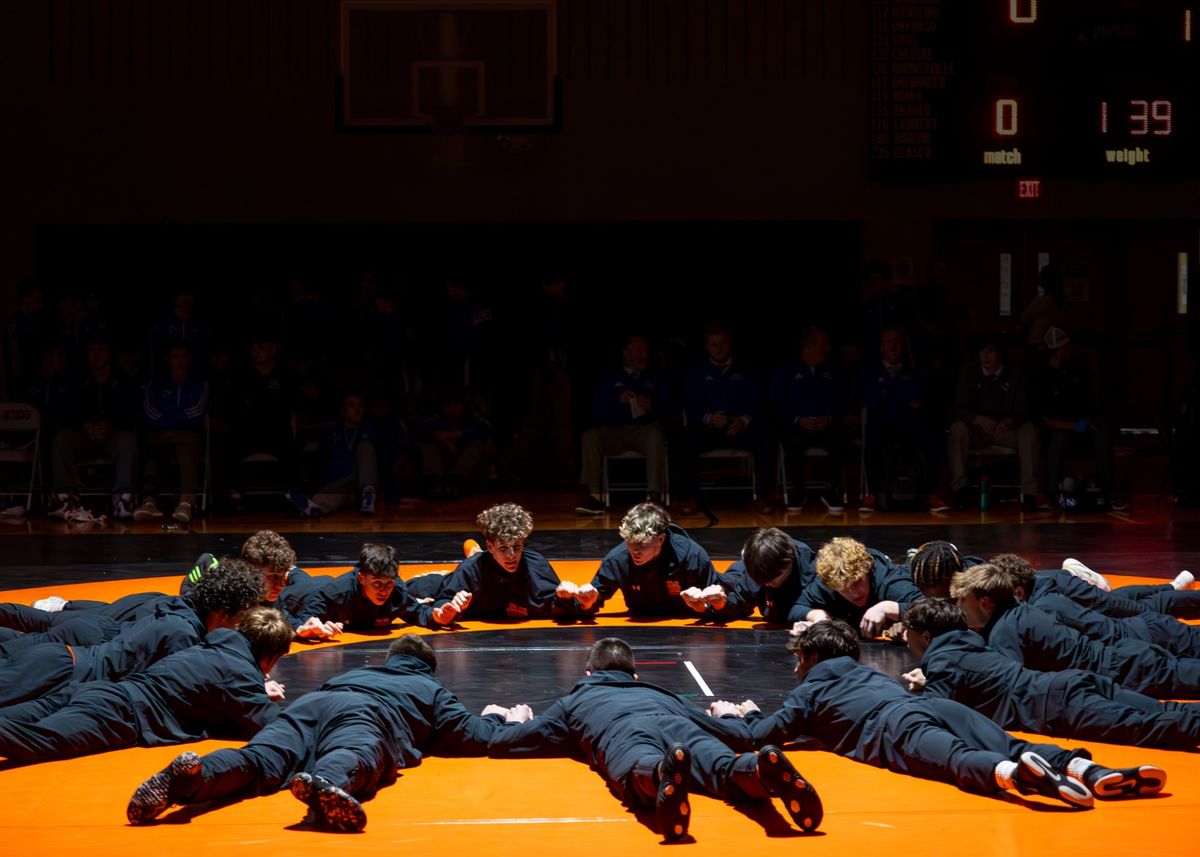 Northampton wrestlers lie in a circle on the orange home mat with their fists together before a match