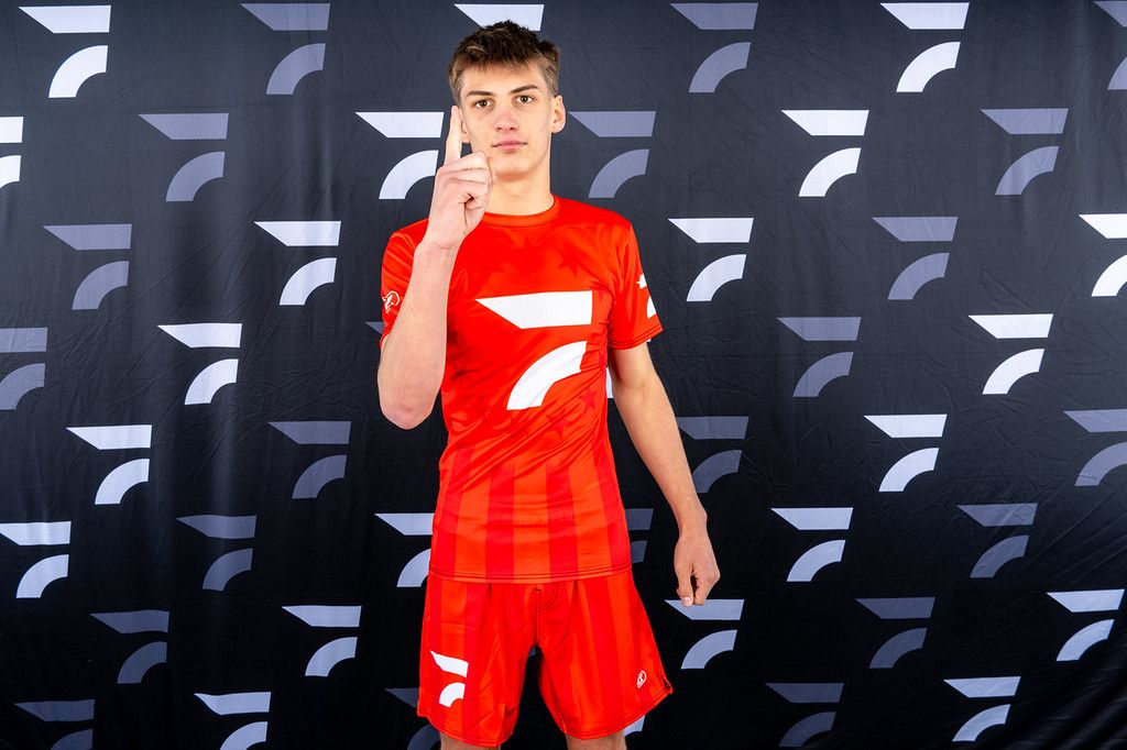 Brayden Wenrich in a red FloWrestling shirt holds up one finger in front of a FloWrestling backdrop